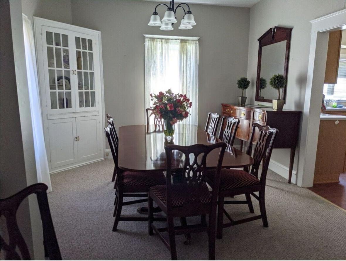 The Alumni House dining room with a wooden dining table with eight chairs, a wooden hutch with mirror, a corner china cabinet, and a vase full of flowers.